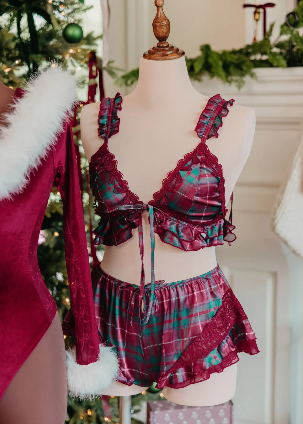 Satin Ruffle Bralette - Tartan. A holiday Christmas themed classic plaid in red and green.  ruffled lingerie top, featuring lace bow trim, ruffled-tie adjustable shoulder straps. 

High Waist Satin Flutter Shorts - Tartan. A pair of Christmas plaid satin shorts featuring a ruffled hem, sheer bow lace side panels, and a front key hole with bow details

A two-piece lingerie displayed on a female mannequin torso in front of a Christmas tree. Part of a mannequin wearing a red velvet Santa teddy can be seen.