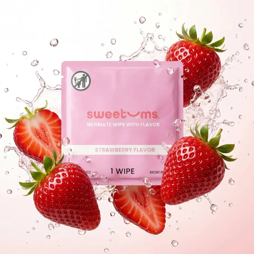 A pink Sweetoms Intimate Wipe packet with strawberry flavor, surrounded by fresh whole and sliced strawberries and water splashes on a pale pink background.
